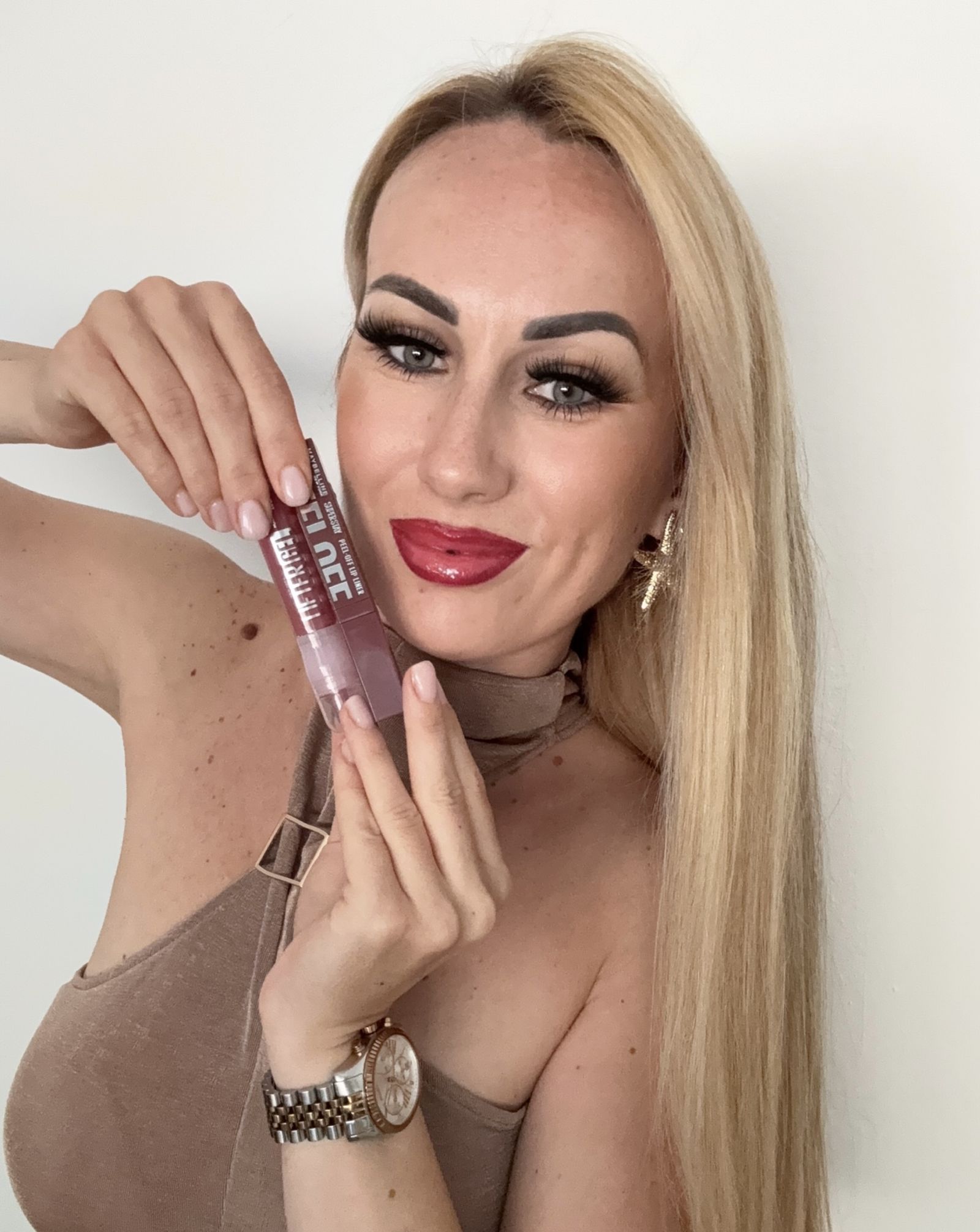 Emina hält zwei Lippenprodukte an ihr Gesicht